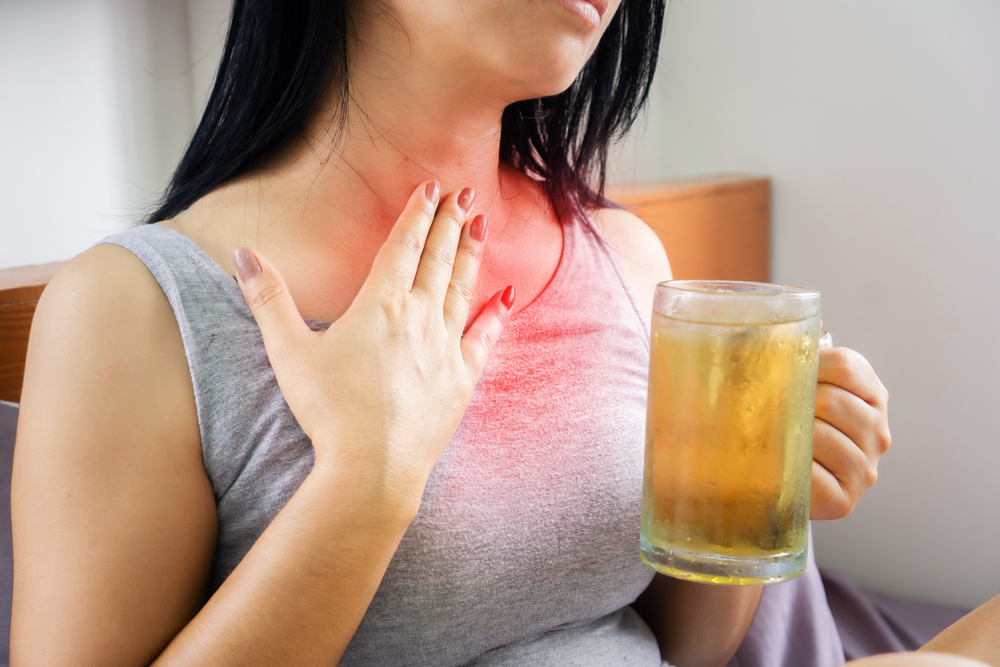 woman holding chest in pain while drinking beer