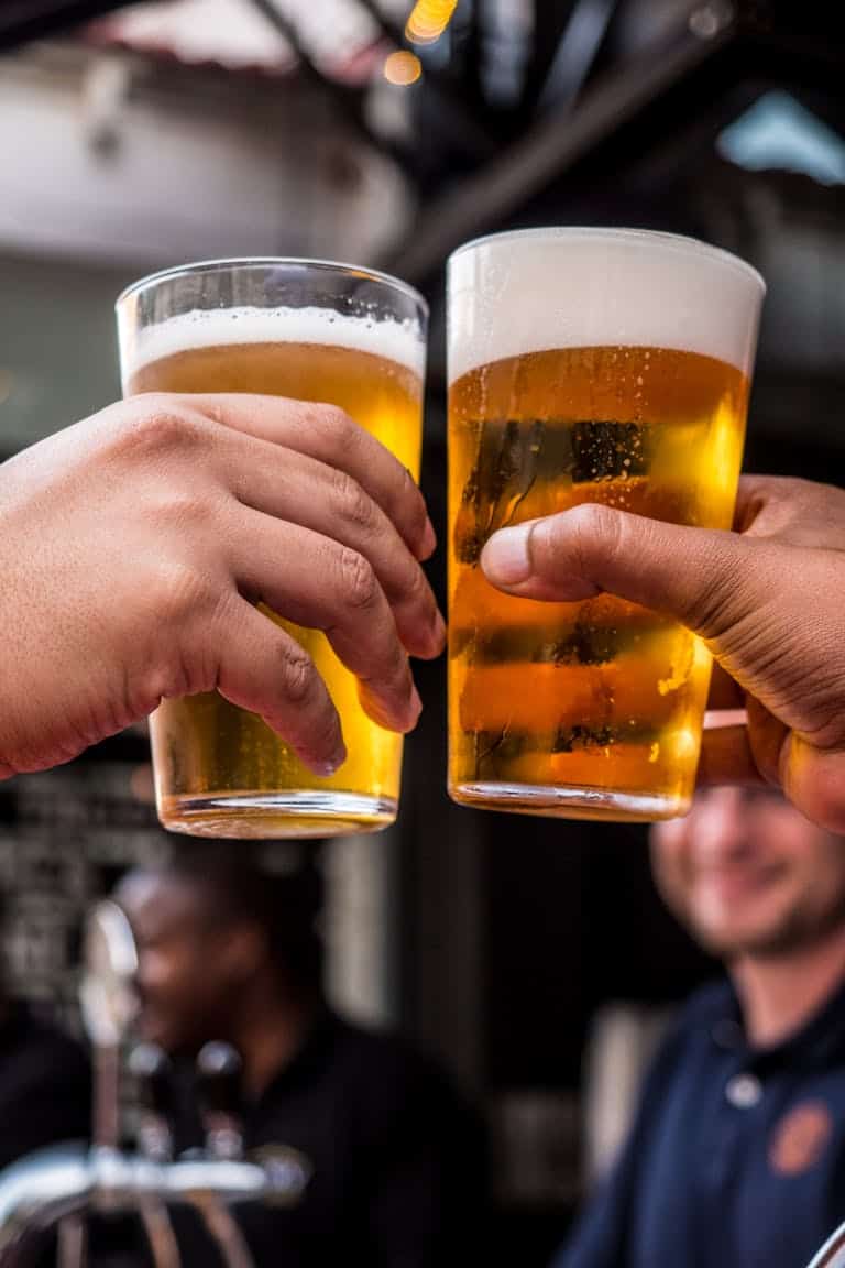 Close-up of two friends toasting with cold beer glasses at a lively bar, celebrating friendship and good times.