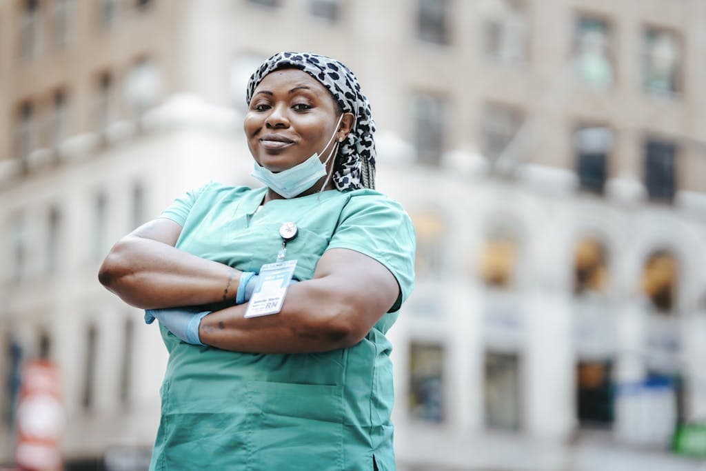 Proud nurse with arms crossed, in uniform, outdoors, urban setting, showing confidence and professionalism.