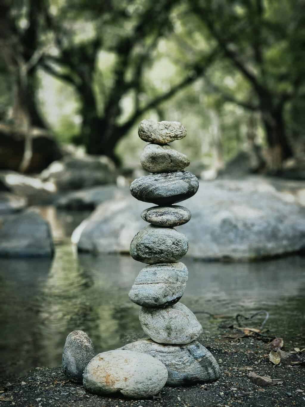 A serene stack of stones balanced beside a peaceful stream in a wooded environment.