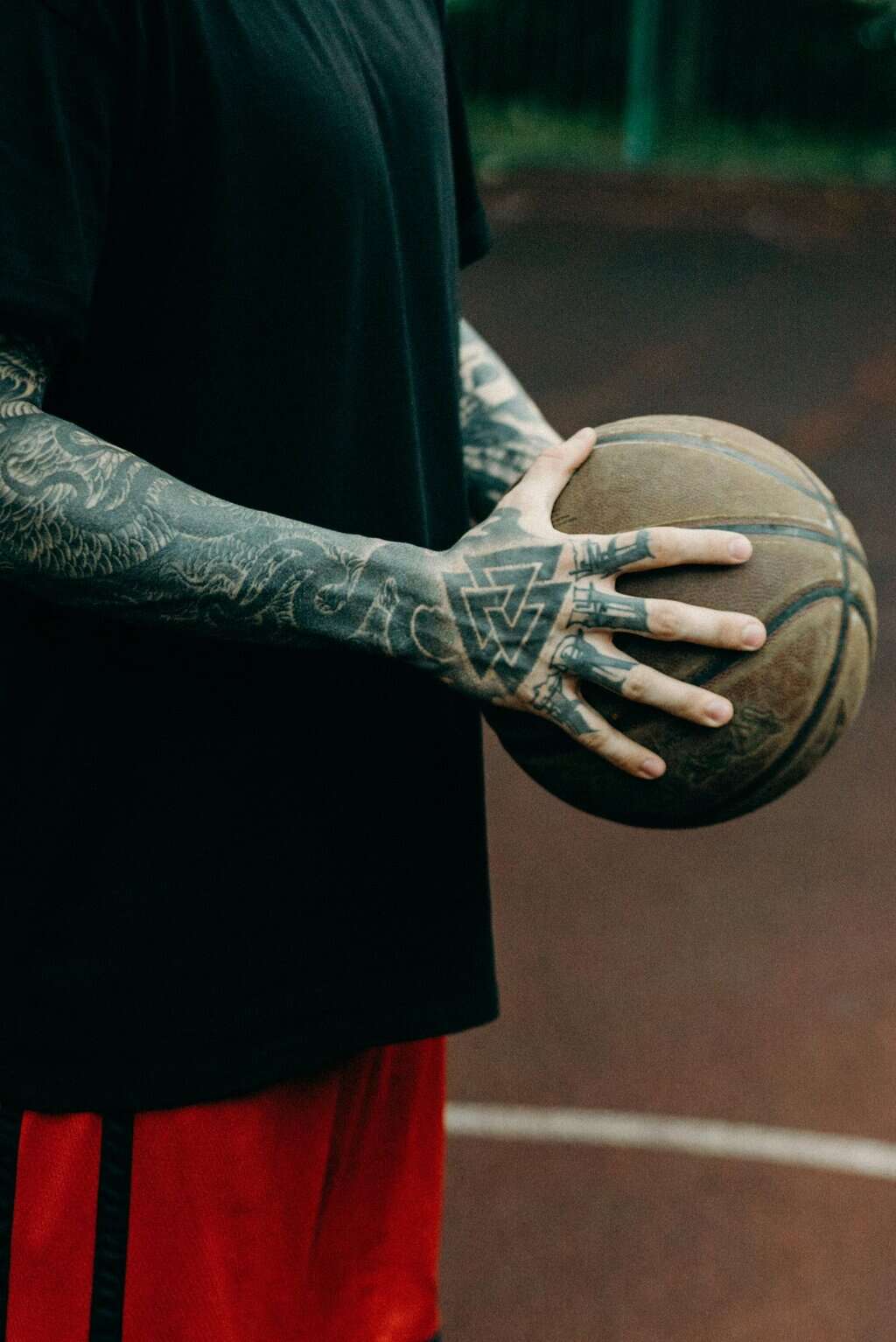Close-up of a tattooed athlete holding a basketball on an outdoor court.