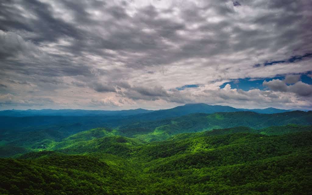 Scenic mountain landscape with rolling green hills under a dramatic cloudy sky.